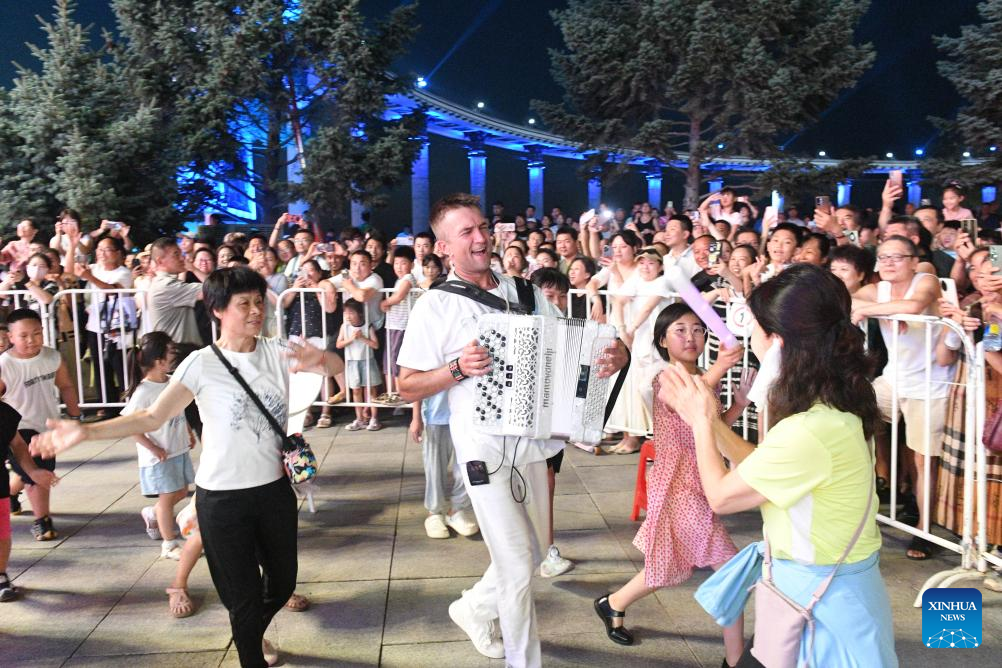 Pelancong berinteraksi dengan seorang pemain alat muzik akordion dari Rusia di sebuah dataran di Harbin, Provinsi Heilongjiang, timur laut China pada 22 Julai 2025. (Xinhua/Liu Yang)