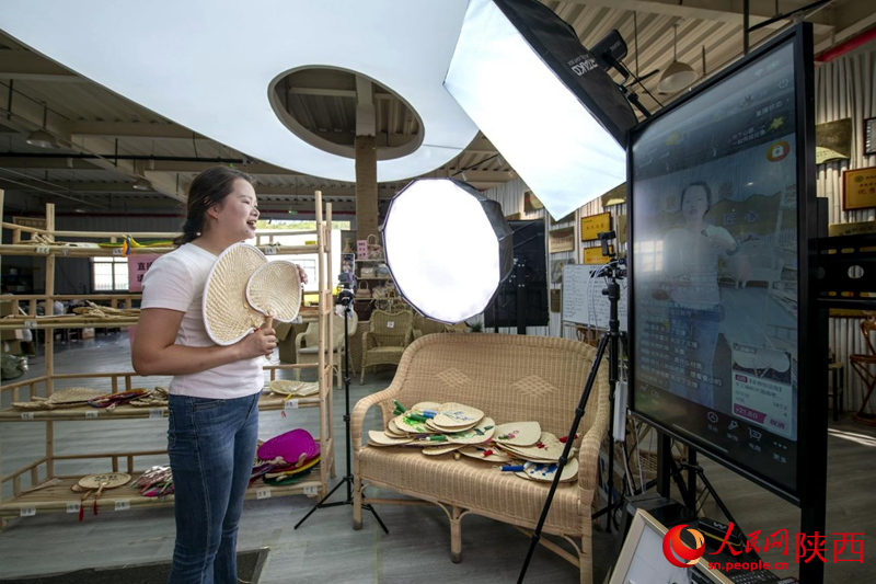 Seorang juruacara penstriman langsung memperkenalkan kerja kraf anyaman kipas rotan semasa promosi di Syarikat Shaanxi Liangshun Jiangxin Industry yang berpangkalan di perbandaran Huangguan, daerah Nanzheng, Hanzhong, Provinsi Shaanxi, barat laut China. (People’s Daily Online/Weng Qiyu)