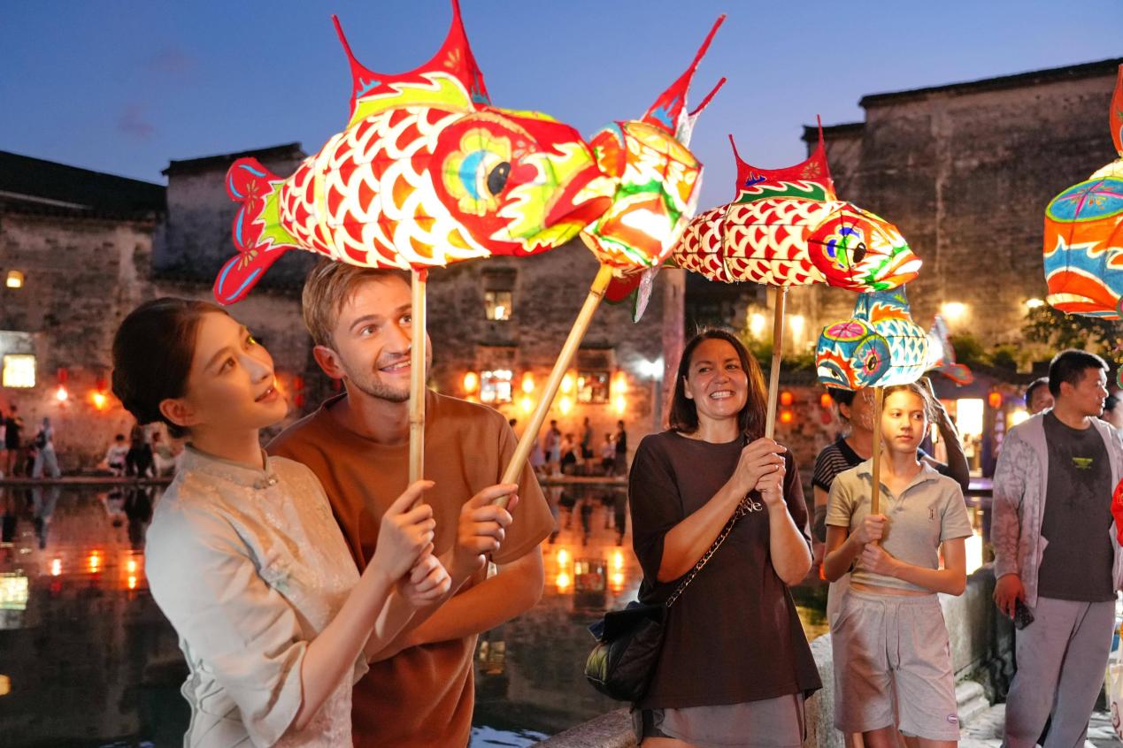 Imej bertarikh 5 Julai 2025 ini memperlihatkan pelancong asing sedang merasai pengalaman perarakan tanglung berbentuk ikan di kampung Hongcun, kaunti Yixian, Huangshan, Provinsi Anhui di timur China. (Foto oleh Xu Jiadong)